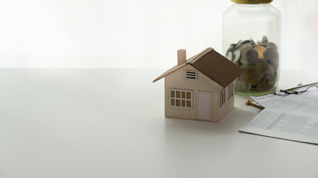Modellhaus neben einem Sparglas mit Münzen